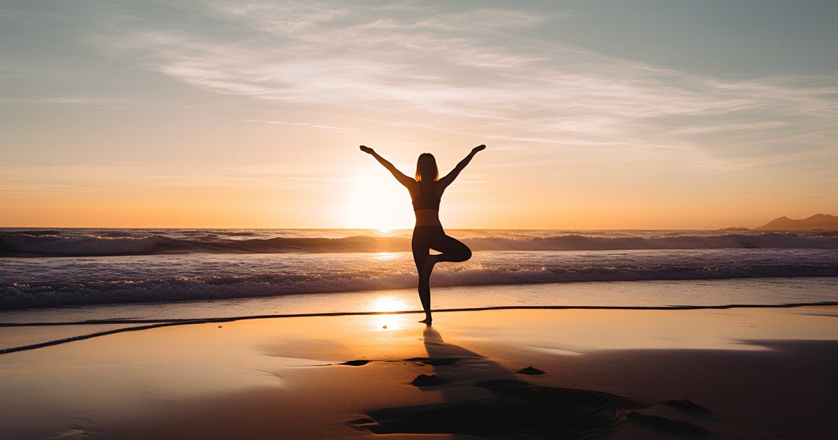 A woman in a lotus pose on the sandy beach facing the sunrise